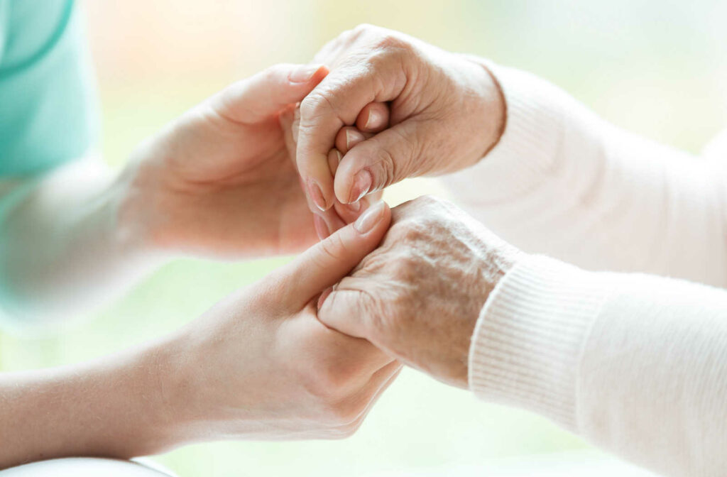 A young woman holding an elderly person's hand as she assists them in daily activities.