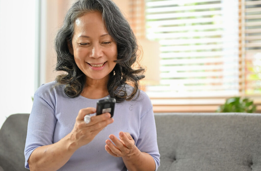A senior woman smiling and checking her blood sugar level using a glucometer and test strip at home