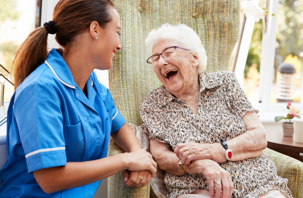 A senior woman sitting in a chair and talking to a caregiver in a senior living community.