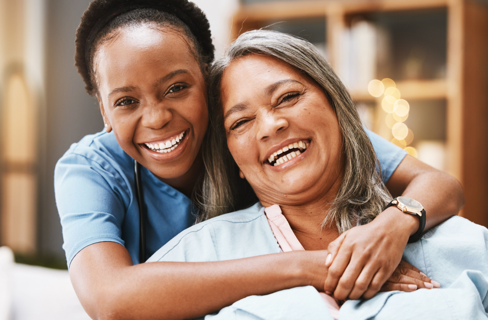 A caregiver and an older adult woman smiling while looking directly at the camera.
