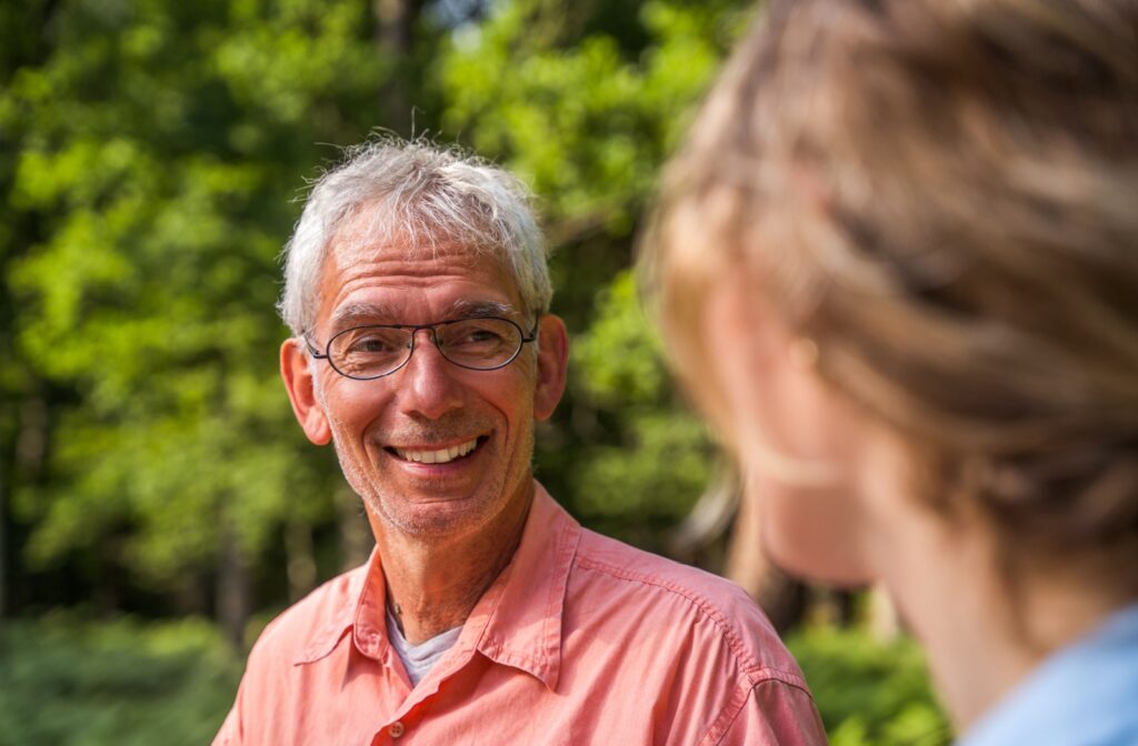 An older adult man with his daughter, smiling and talking in a park