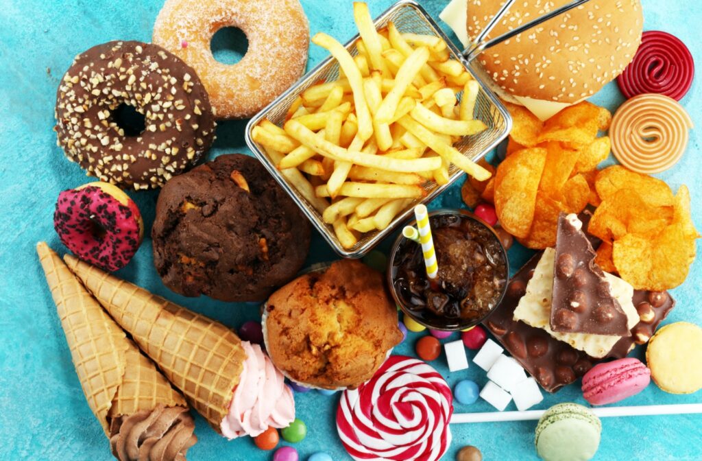 An assortment of unhealthy foods like chips, fries, donuts, and candy laid out on a table.