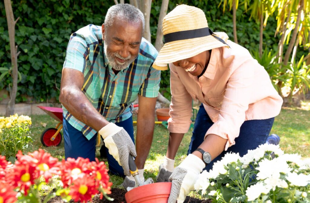 An elderly couple smiling and planting flowers outdoors.